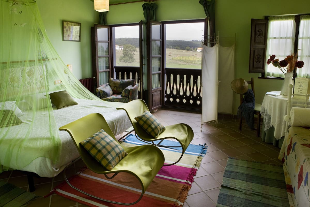 A bedroom with a bed, two chairs, a table, and a view of the outdoors.