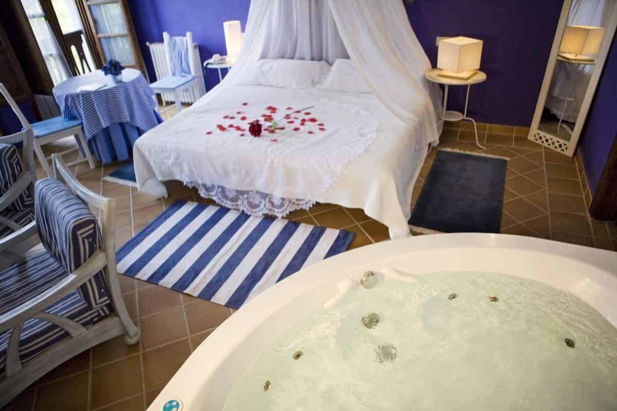 A bedroom with a bed, a bathtub, and a chair.
