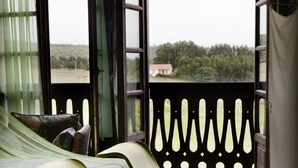 A room with a bed, two rocking chairs, a colorful striped rug, and a balcony with a view of trees and a house. - Hotel Rural La Llosa de Fombona (Gozon)
