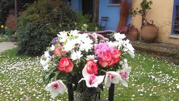 Traditional building with a tiled roof, surrounded by a garden with a wooden chair and a vase of fresh flowers.
