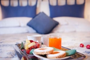 A breakfast tray with fruits, pastries, and orange juice on a bed with a blue pillow. - A Due Passi (Forte dei Marmi)