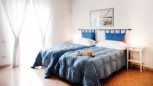 A bedroom with two beds, a nightstand, a painting on the wall, and a window with curtains. - A Due Passi (Forte dei Marmi)