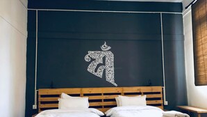 Cama doble con cabecera de madera y dos almohadas, un adorno en la pared y una mesita de noche.