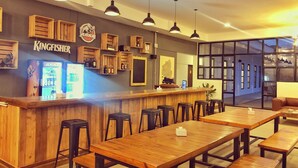 Zona de bar con muebles de madera, iluminación colgante y un letrero que dice "Kingfisher".