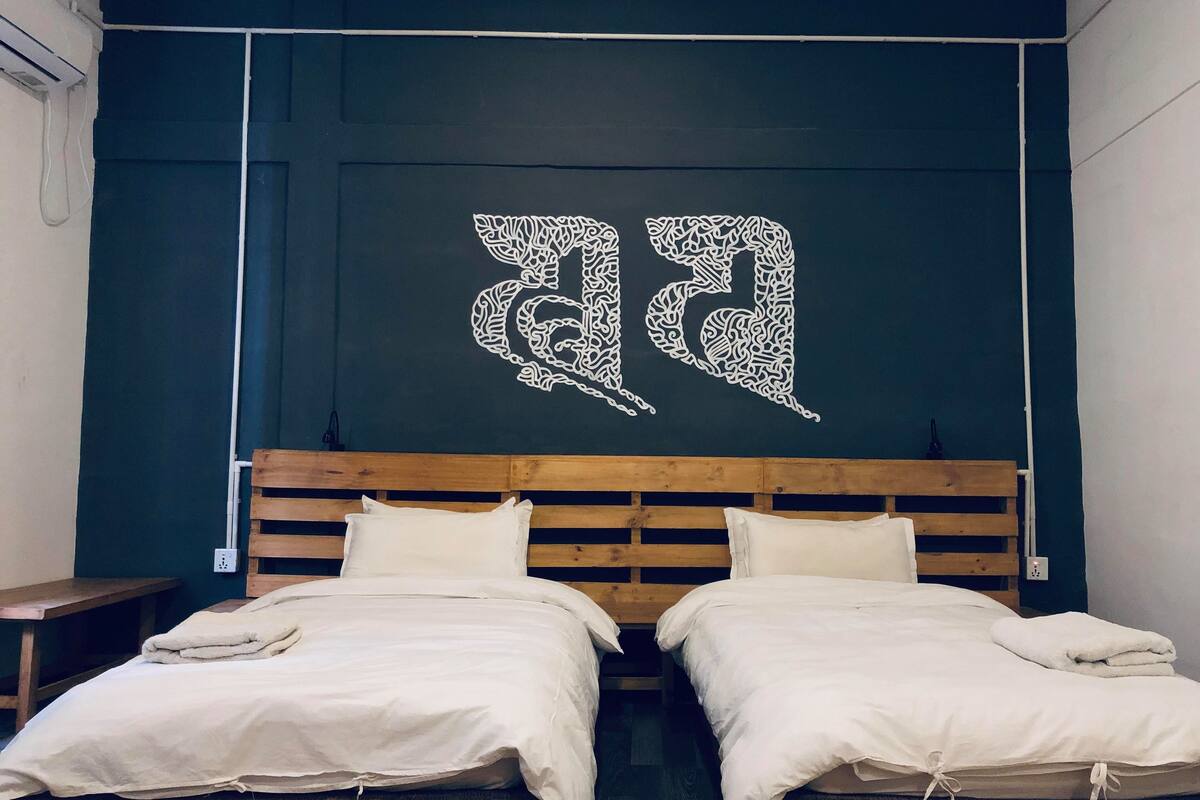 A room with two beds, a dark wall with a white abstract design, and a wooden headboard.