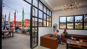 Un espacio interior con ventanas amplias, un sofá de cuero marrón, una mesa de madera y un ventilador.