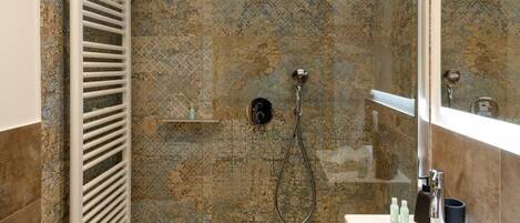A modern bathroom with a glass-enclosed shower, a white vanity with a mirror, and a towel on the floor.