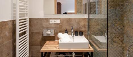Un baño moderno con ducha de vidrio, tocador de madera con lavamanos y un inodoro.