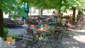 An outdoor café with multiple tables and benches, surrounded by trees and a stone pavement. - Gasthof Messerschmied (Grassau)