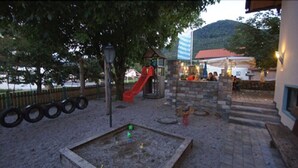 A playground with a slide and climbing structures, a sandbox, and a building with a red roof in the background. - Gasthof Messerschmied (Grassau)