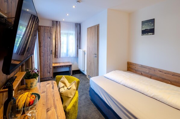 A hotel room with a bed, a desk with a computer, a chair, a TV, and a window with curtains. - Gasthof Messerschmied (Grassau)