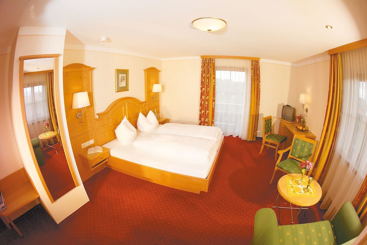 Une chambre d’hôtel avec un grand lit, un bureau avec une télévision, une chaise et une petite table sur laquelle est posé un vase.