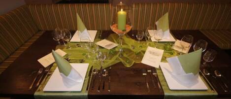 A dining table set for four with green tablecloths, clear glassware, and a lit candle centerpiece.