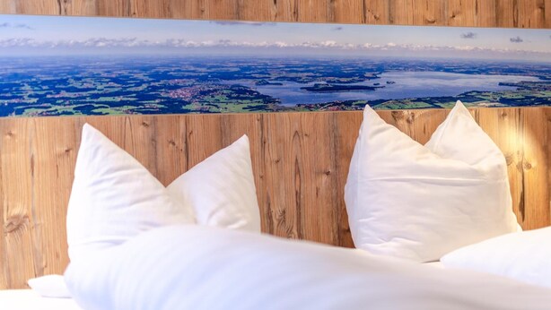 A bed with white bedding and pillows, set against a wooden wall with a scenic landscape mural above it. - Gasthof Messerschmied (Grassau)