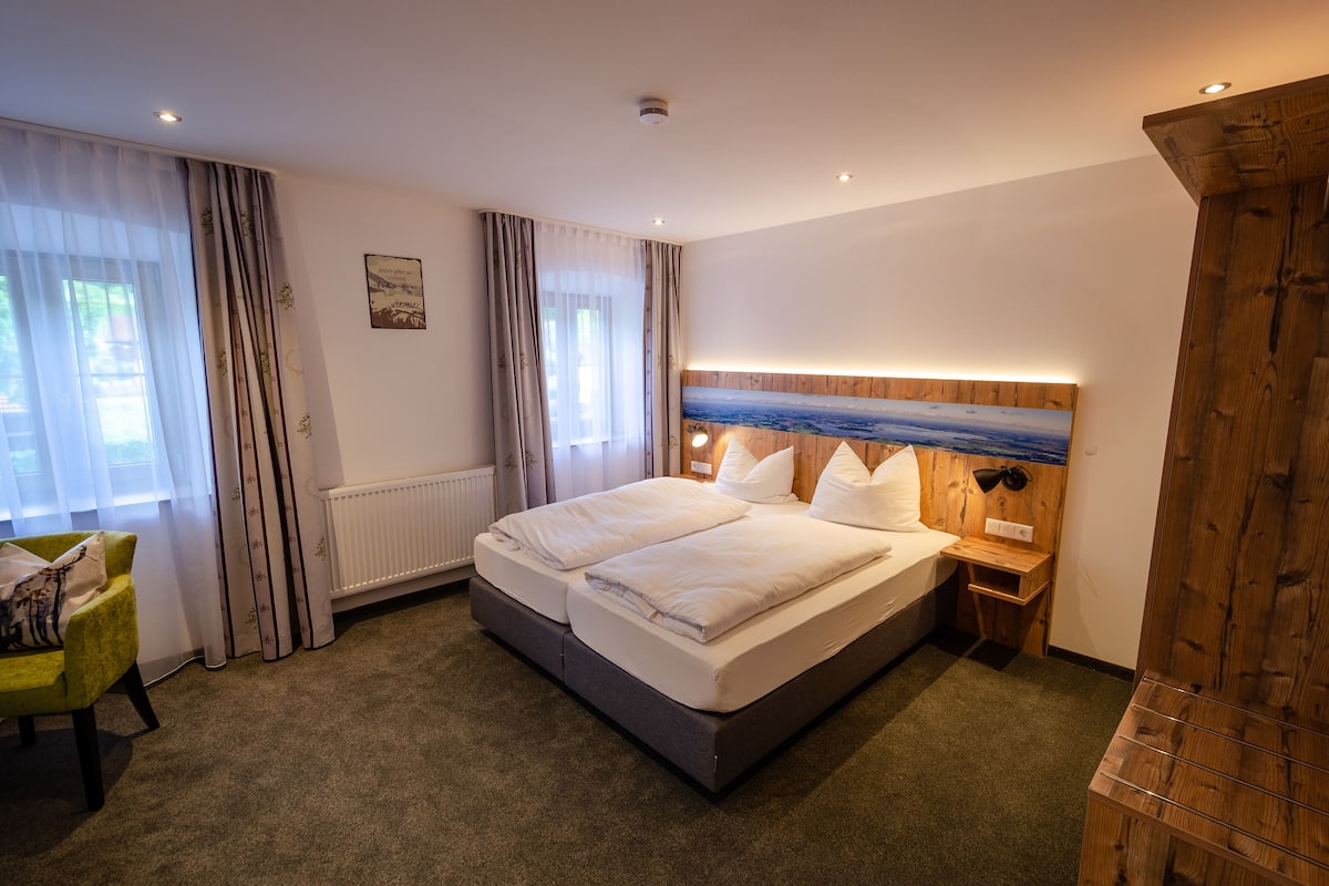 Une chambre d’hôtel avec un grand lit, une tête de lit en bois, une table de chevet, une chaise et une vue sur l’extérieur par la fenêtre.