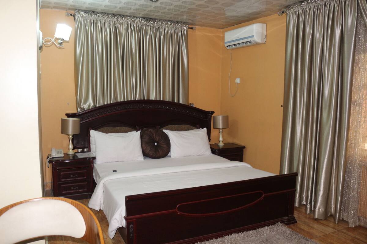 Un dormitorio con una cama de madera, dos mesitas de noche, una lámpara, una silla y aire acondicionado instalado en la pared.