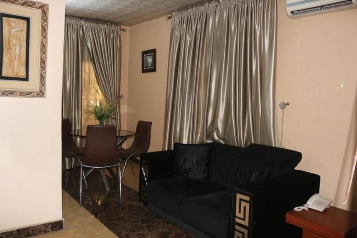 Una habitación con un sofá negro, una mesa de comedor con sillas, una planta en maceta y un cuadro en la pared.