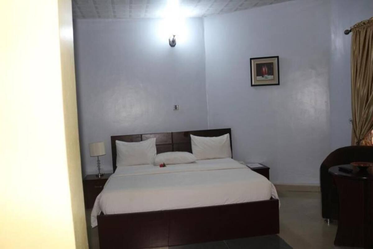 Habitación de hotel con una cama individual, una mesita de noche, una lámpara, un cuadro en la pared y una silla.