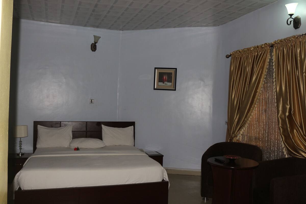 Una habitación de hotel con una cama, una mesita de noche, una lámpara, una silla y una cortina.