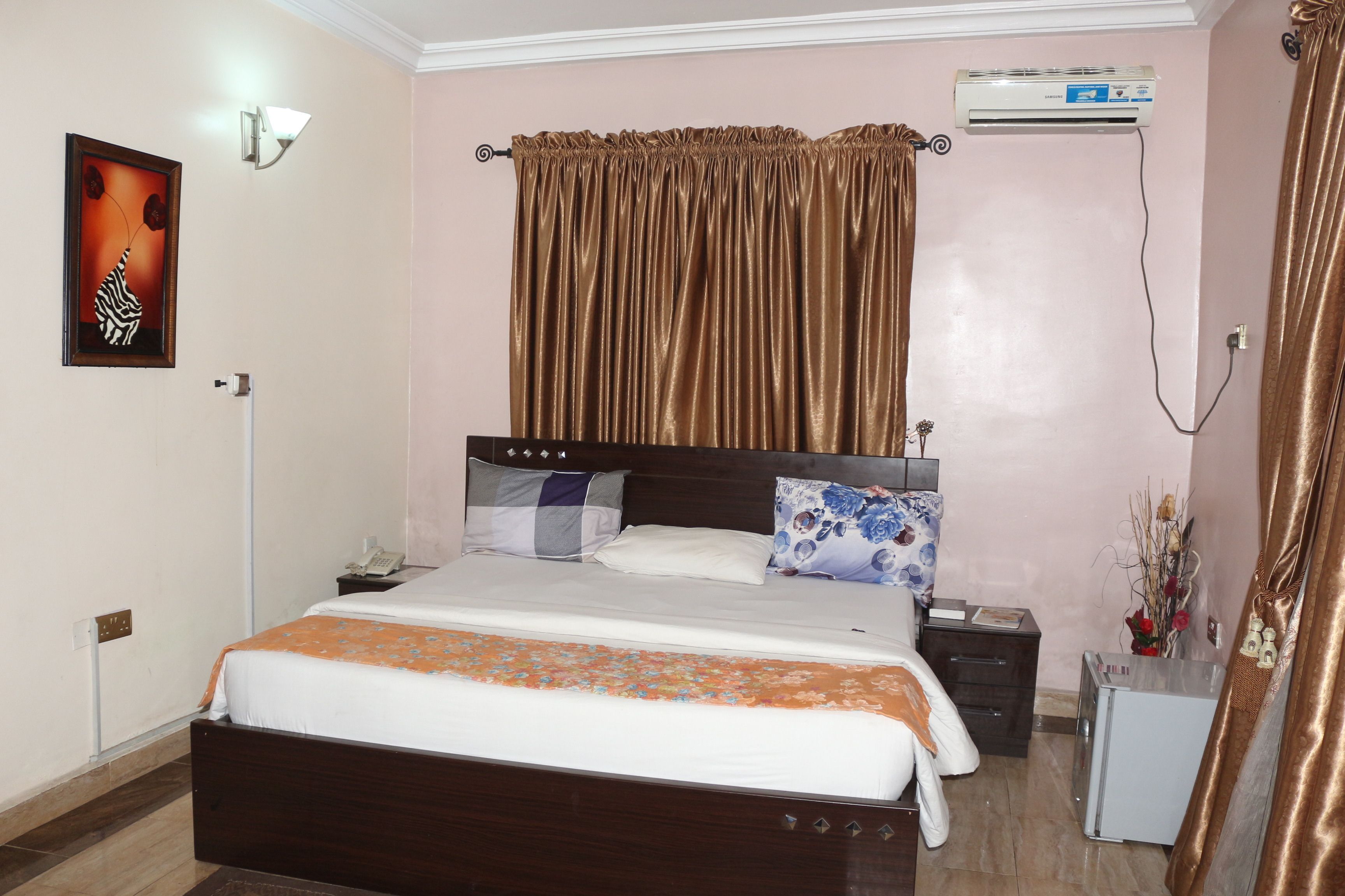 Une chambre à coucher comprenant un lit, une table de chevet, un appareil de climatisation, une commode et une lampe fixée au mur.