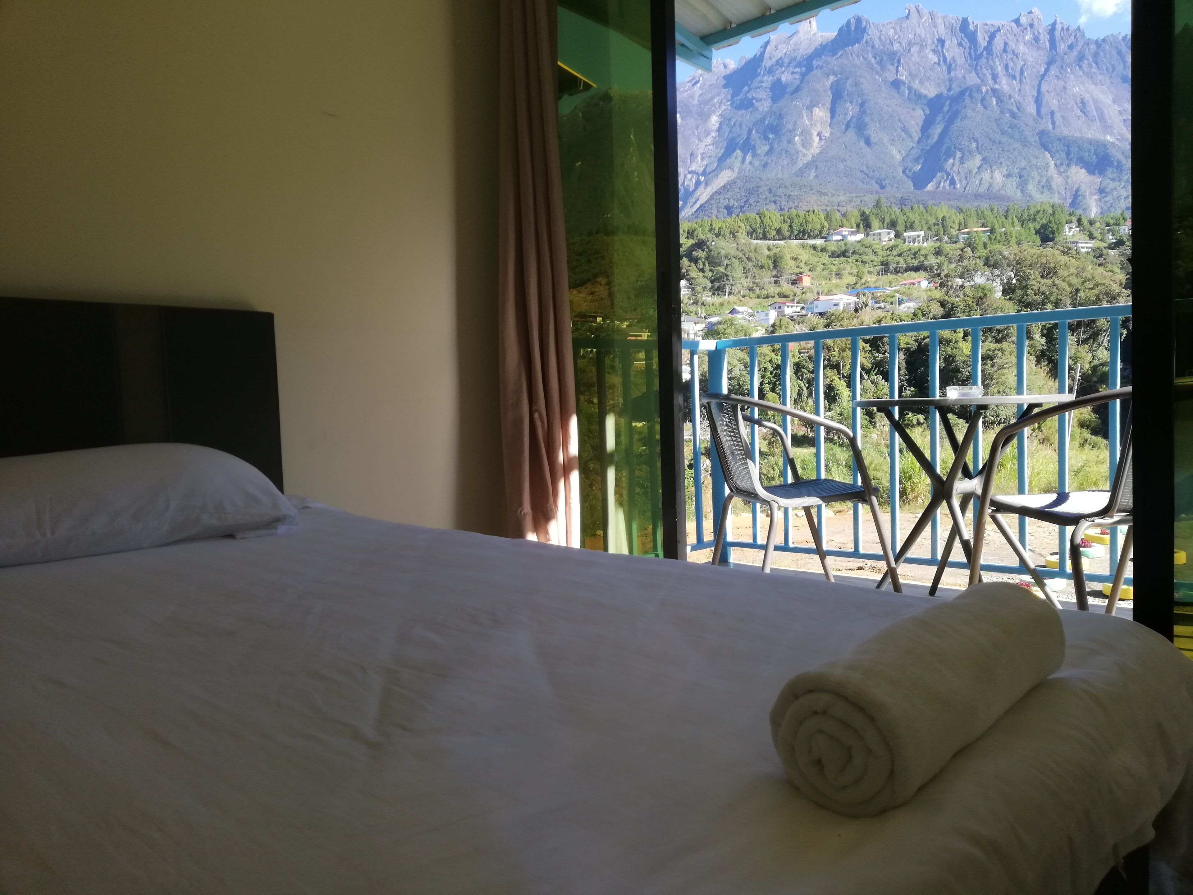 Habitación de hotel con cama, vistas a las montañas y balcón con sillas.
