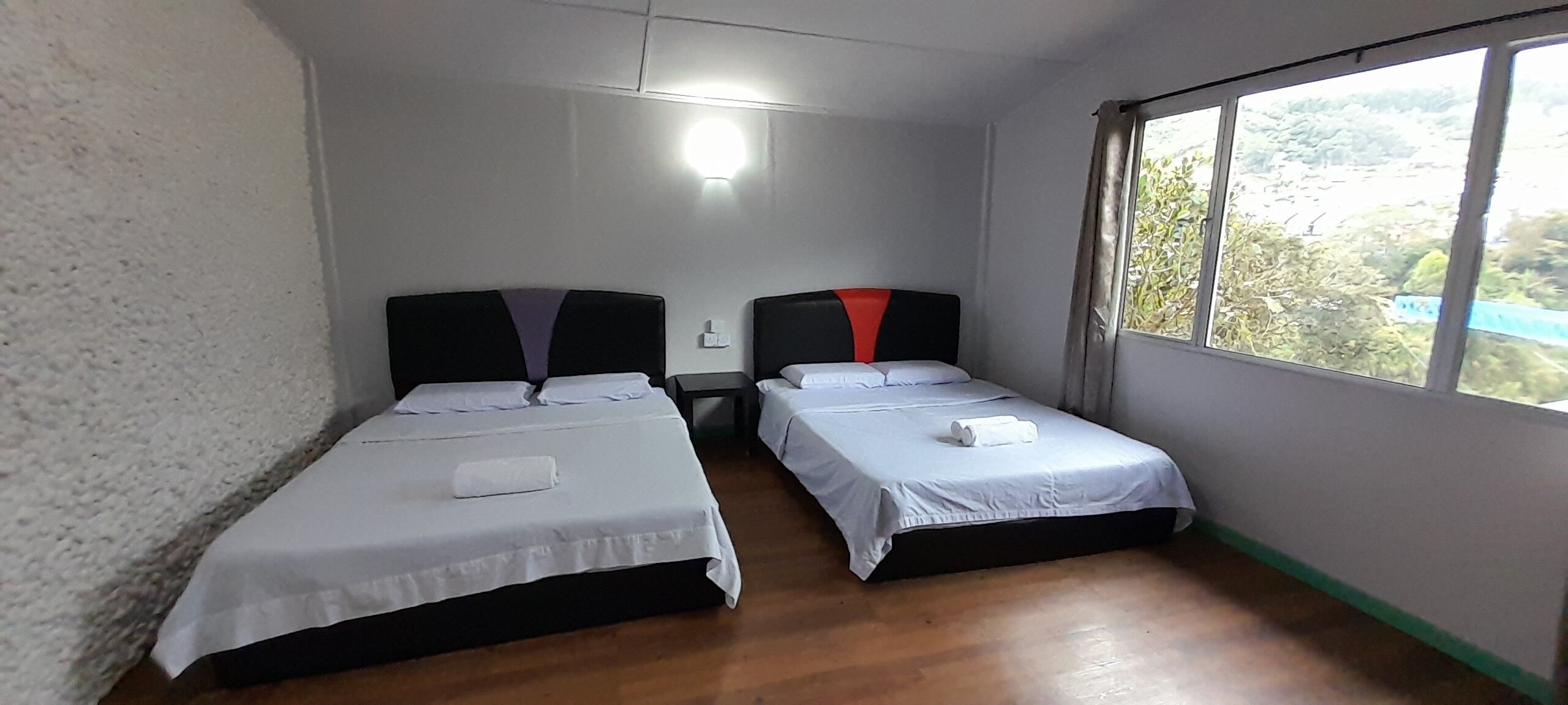 A room with two single beds, a small table, and a window with a view of greenery.