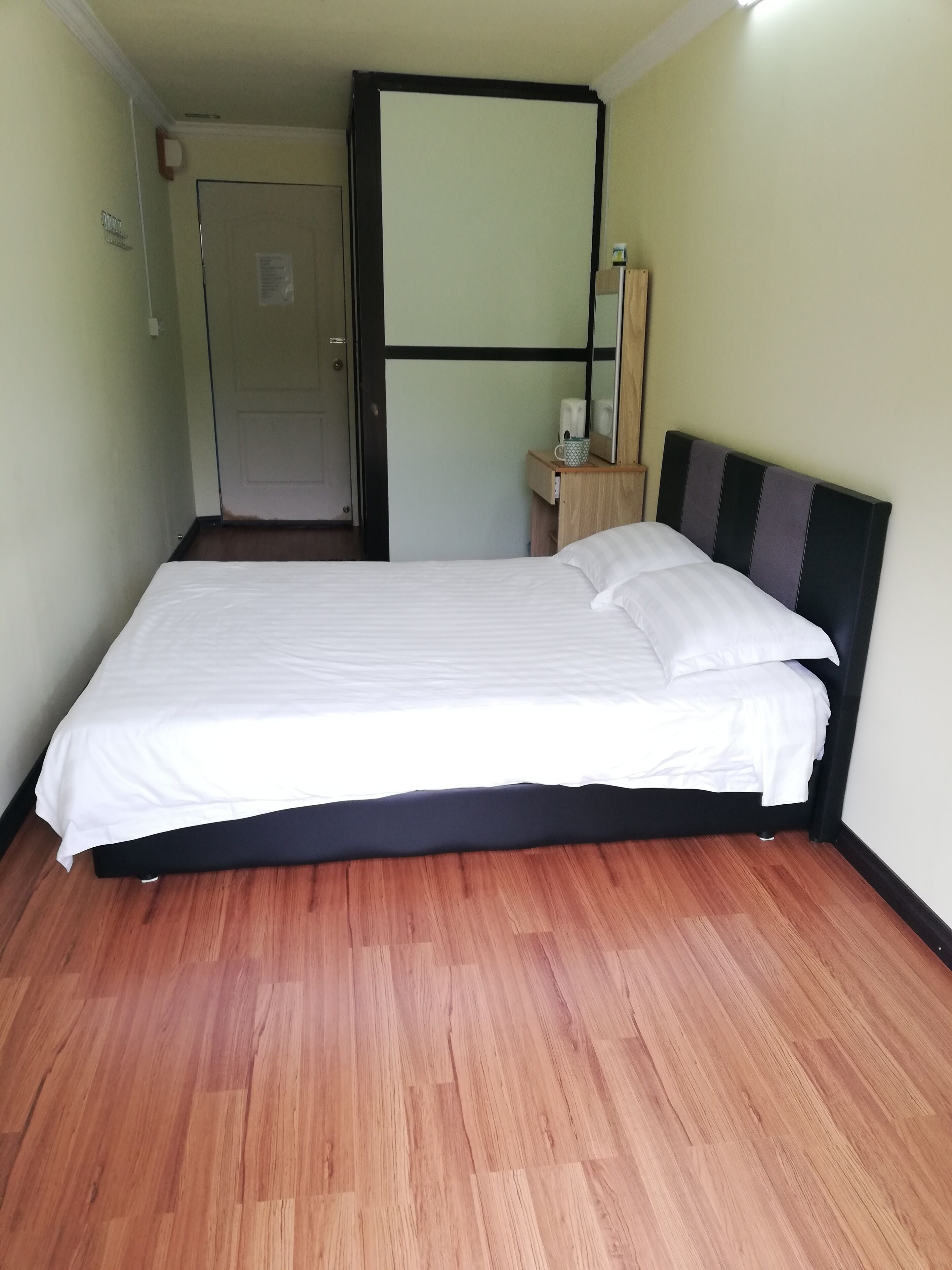 Una cama bien tendida con sábanas blancas en una habitación con suelo de madera y cabecero negro.