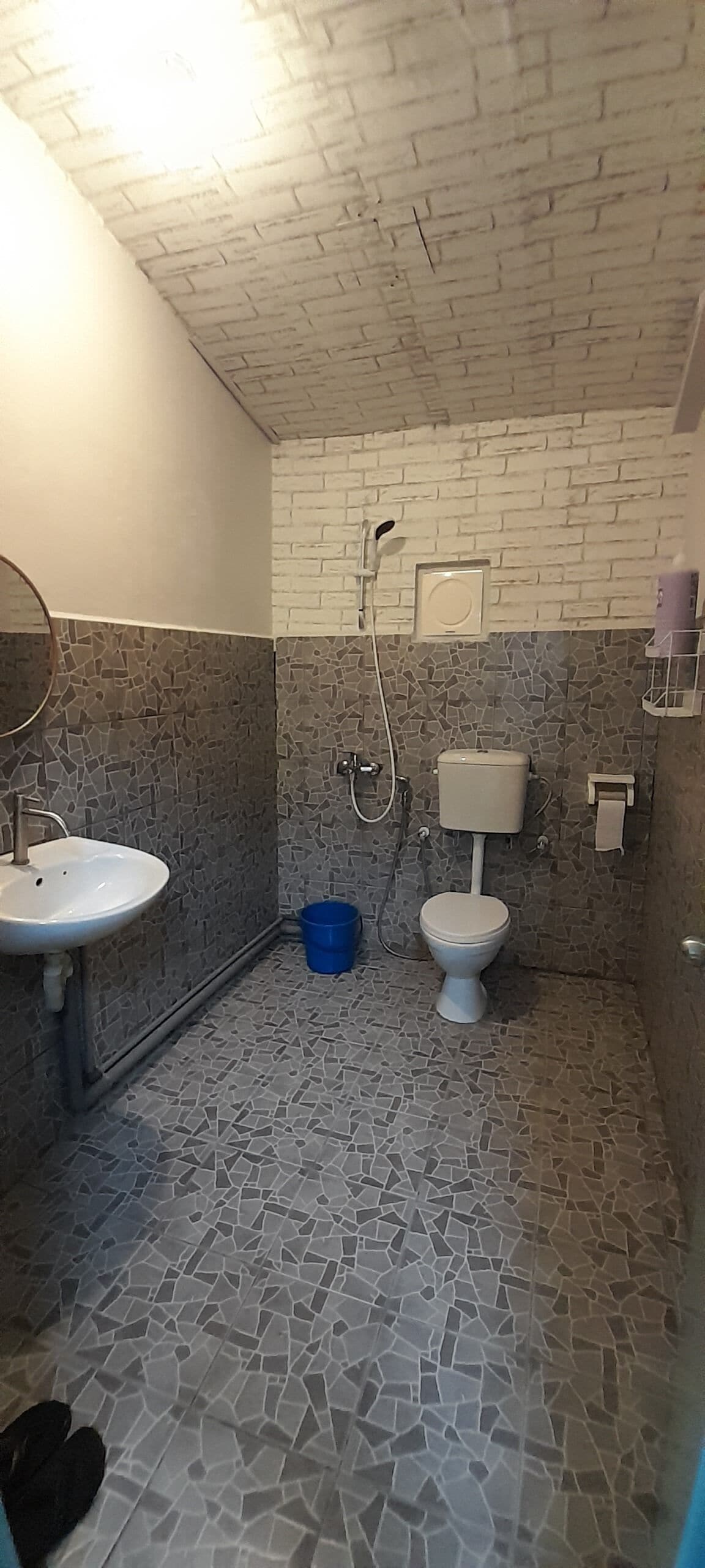 Un baño con lavamanos blanco, inodoro y ducha. El suelo presenta un diseño de mosaico.