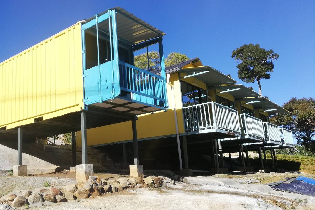 A yellow and blue structure with a balcony, elevated on stilts, surrounded by a rocky landscape.