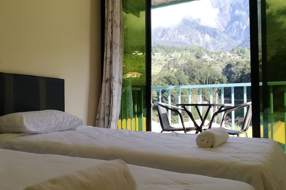 A hotel room with two beds, a balcony with a chair, and a mountain view.