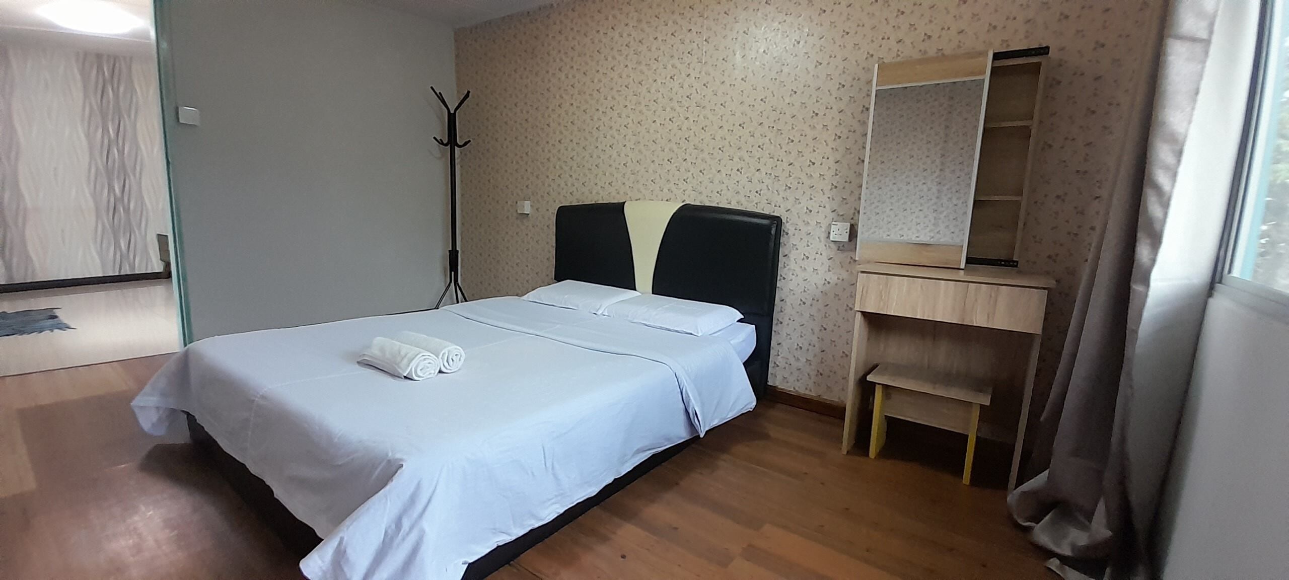 A neatly made bed with white linens and a folded towel, a wooden nightstand with a mirror, and a patterned wall.