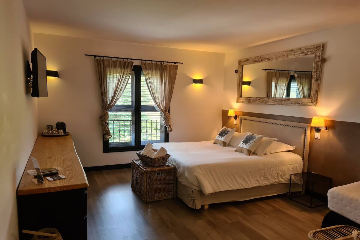 A hotel room with a bed, bedside lamps, a large mirror, a wooden desk, and a wicker basket.