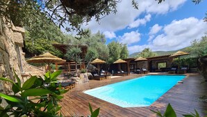 A wooden deck with a swimming pool, lounge chairs, and thatched umbrellas. - Chambre d'Hote Casa Maredda (Albitreccia)