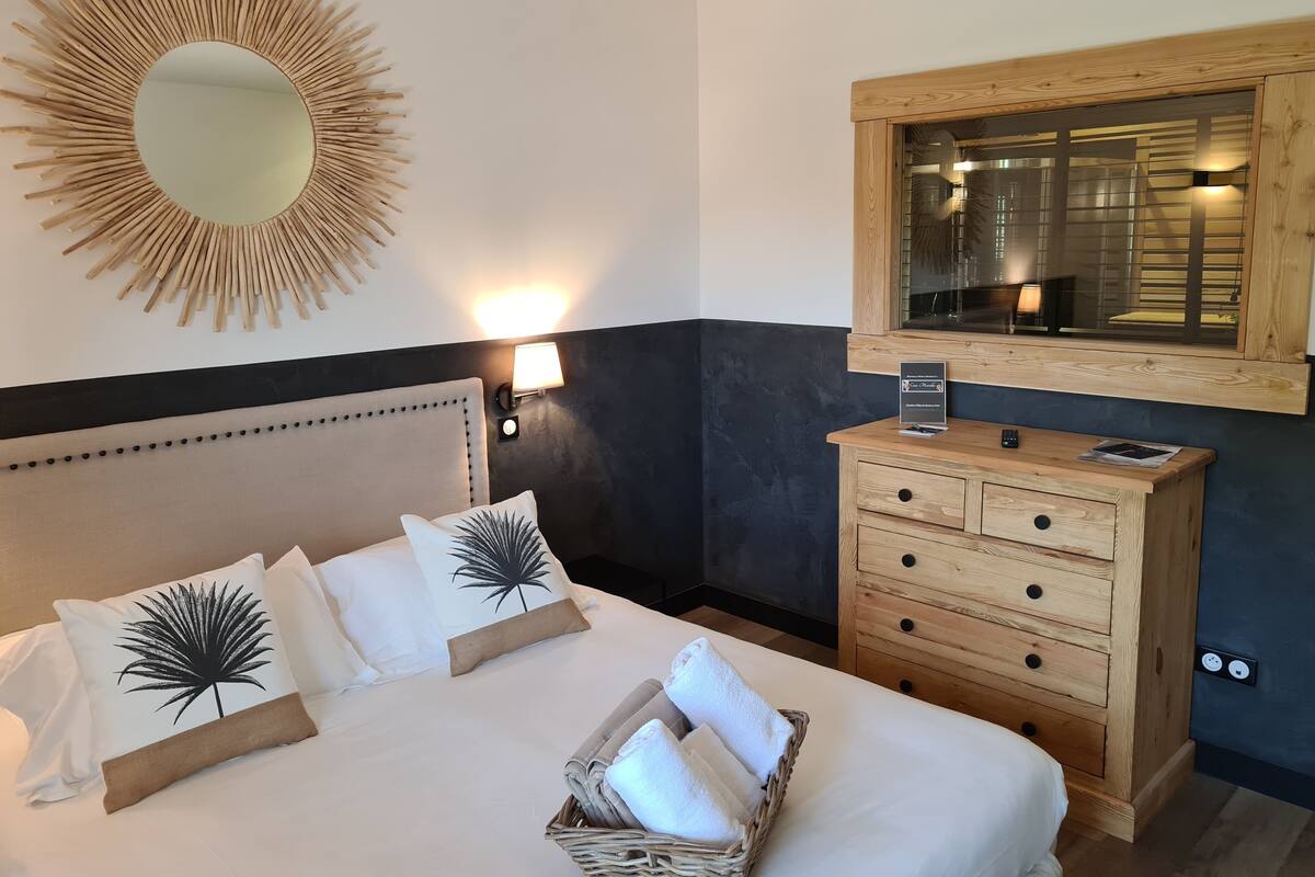 A hotel room with a bed, a wooden dresser, a mirror, and a wall-mounted light fixture.