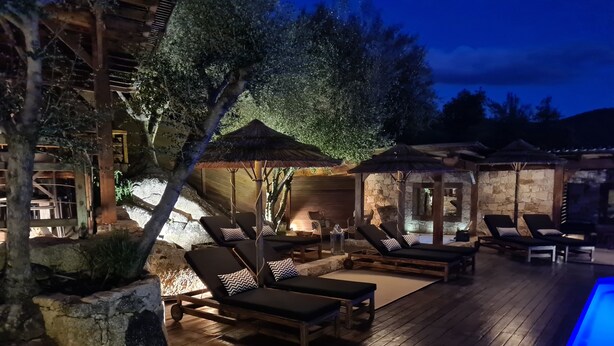 A poolside area with lounge chairs and umbrellas, surrounded by stone walls and wooden deck. - Chambre d'Hote Casa Maredda (Albitreccia)