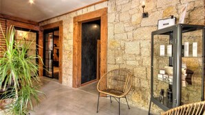 A hallway with stone walls, wooden doors, a wicker chair, and a glass display case with items. - Chambre d'Hote Casa Maredda (Albitreccia)