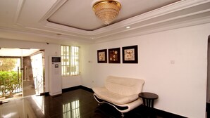 A spacious lobby with a cream-colored sofa, a small round table, and a chandelier. - Belvoir Hotel (Abuja)