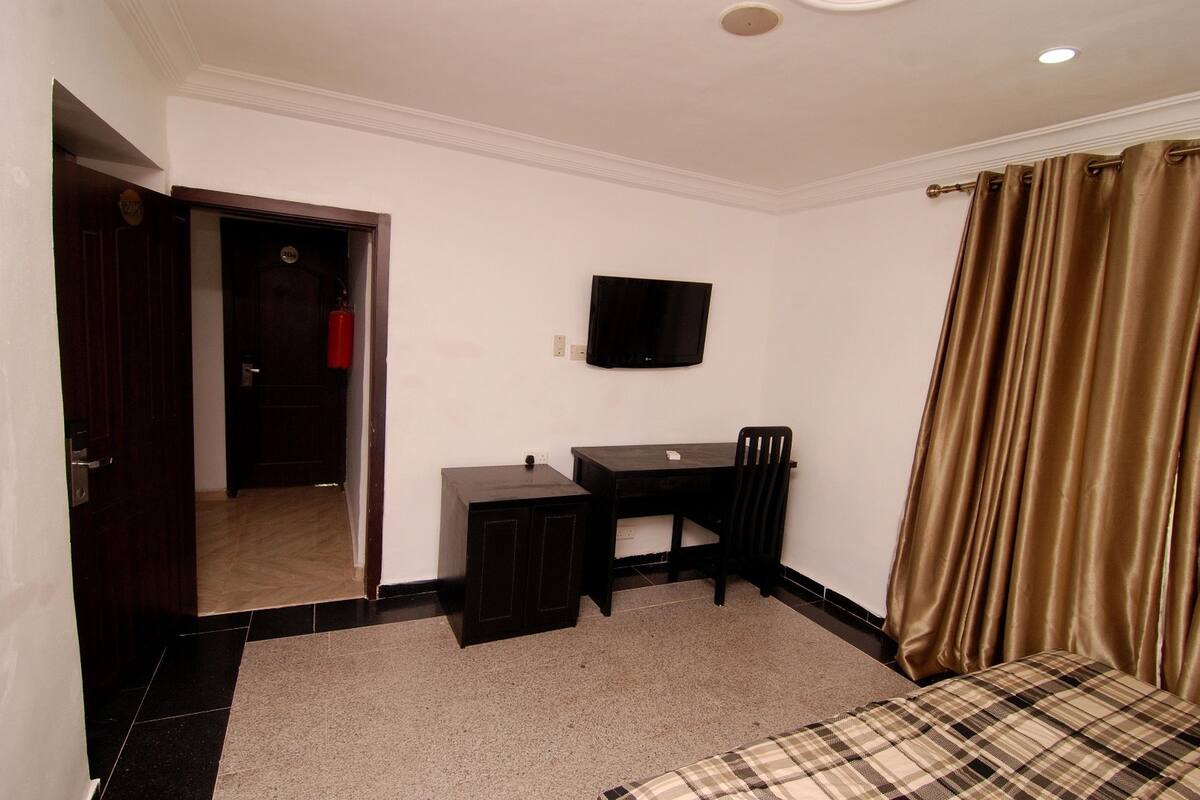 A bedroom with a bed, a desk, a chair, a television, and a door.