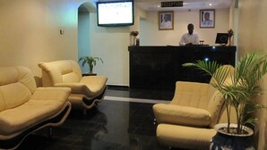 A reception area with a reception desk, two receptionists, and three beige armchairs. - Belvoir Hotel (Abuja)