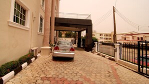 A paved driveway leading to a building with a car parked in front. - Belvoir Hotel (Abuja)