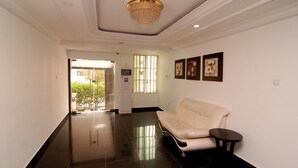A hallway with a white sofa and a small table, a chandelier, and framed artwork on the wall. - Belvoir Hotel (Abuja)