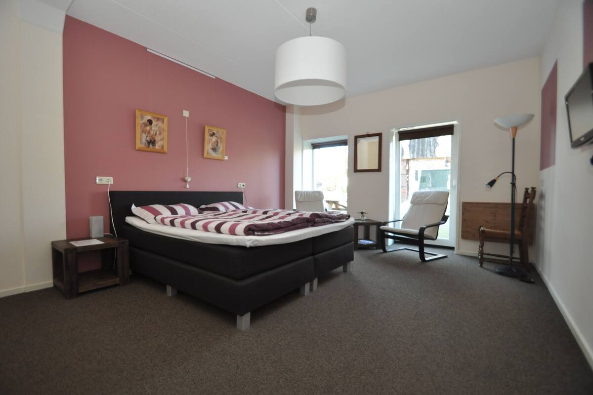 Een slaapkamer met een bed, nachtkastjes, een stoel, een vloerlamp en een raam.