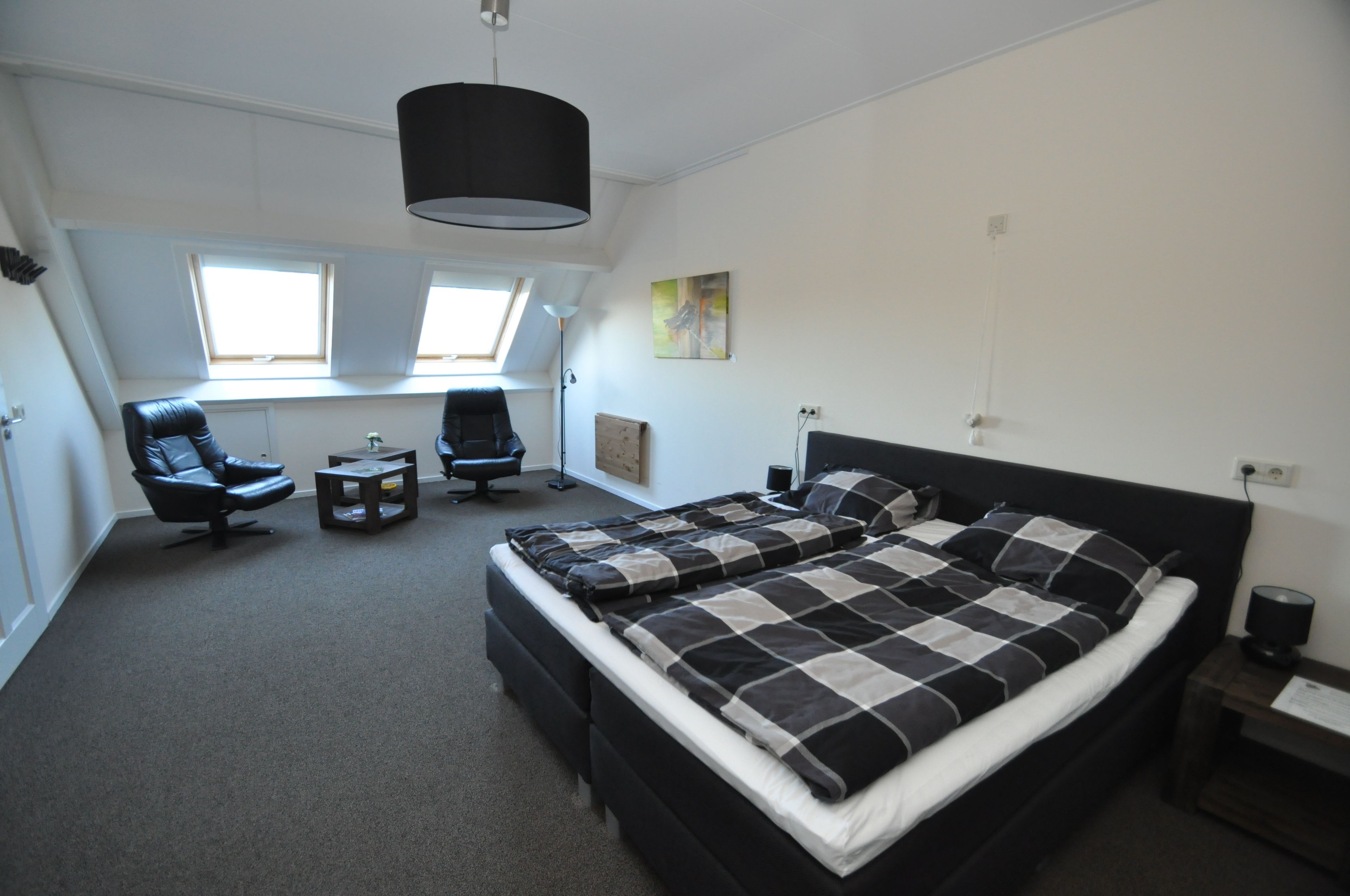 A bedroom with a large bed, two chairs, a small table, a ceiling light, and a window.