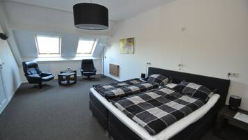 A bedroom with a large bed, two chairs, a small table, a ceiling light, and a window.