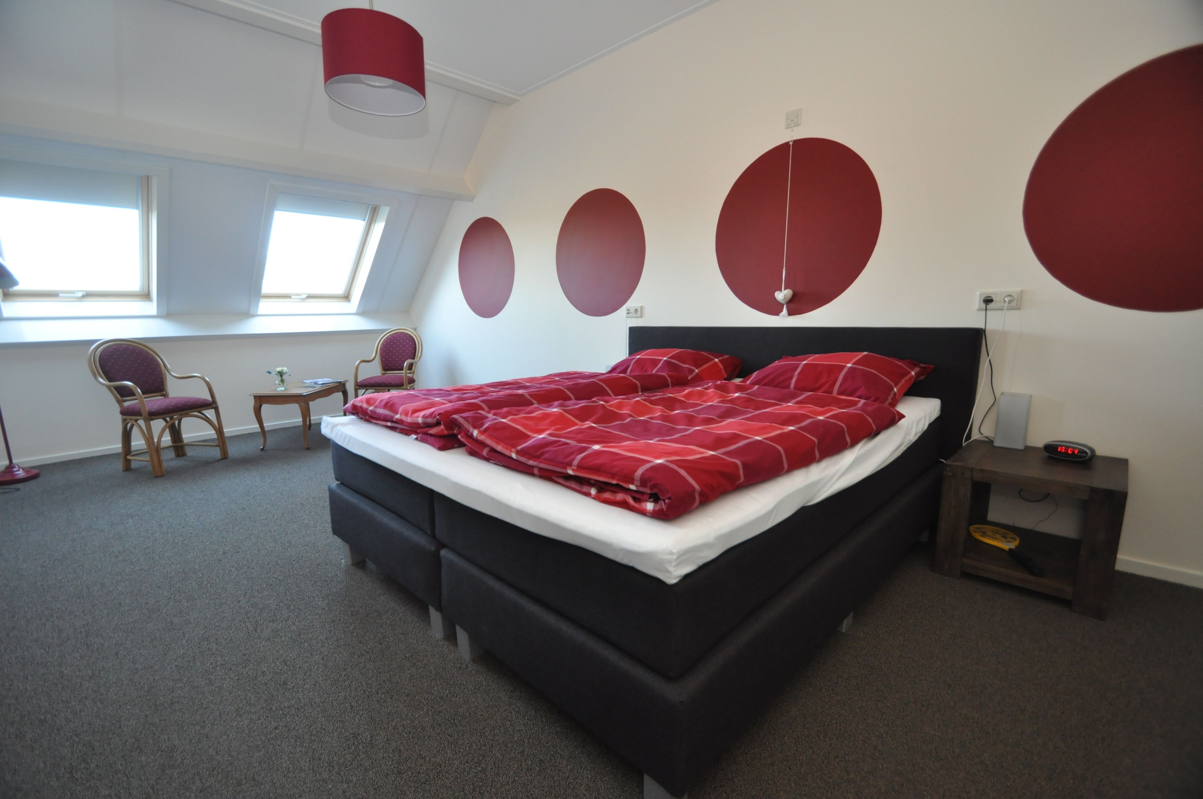 A modern bedroom with a black bed, red bedding, and a skylight window.