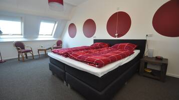 A modern bedroom with a black bed, red bedding, and a skylight window.