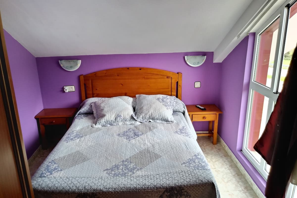 Ein Schlafzimmer mit einem Holz-Kopfteil, einem Bett mit gemusterten Betttextilien, zwei Nachttischen und einem Fenster mit Vorhängen.
