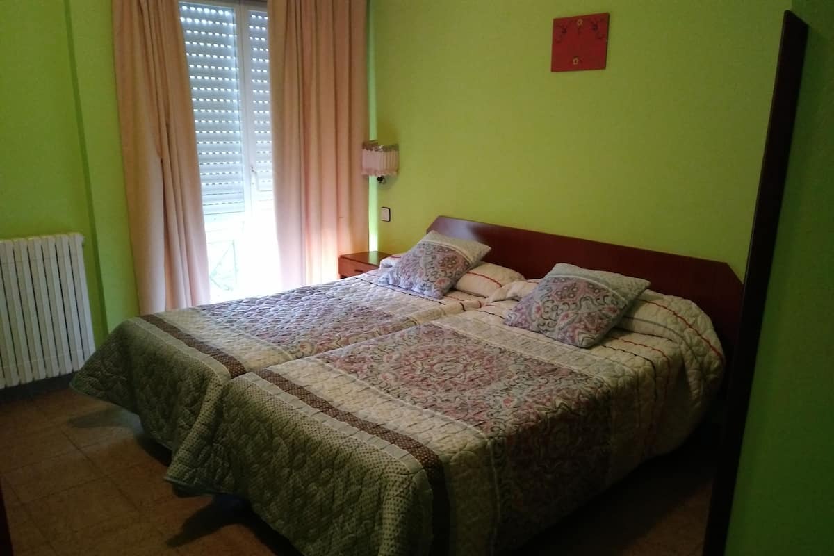 Ein Einzelbett mit gemustertem Bettbezug und Kissen, ein Nachttisch, eine Wandlampe und ein Heizkörper.