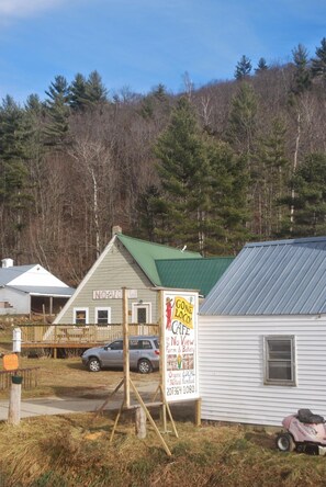 A small building with a green roof, a sign advertising a cafe, and a car parked in front. - No View Farm Inn & Bakery (Rumford)