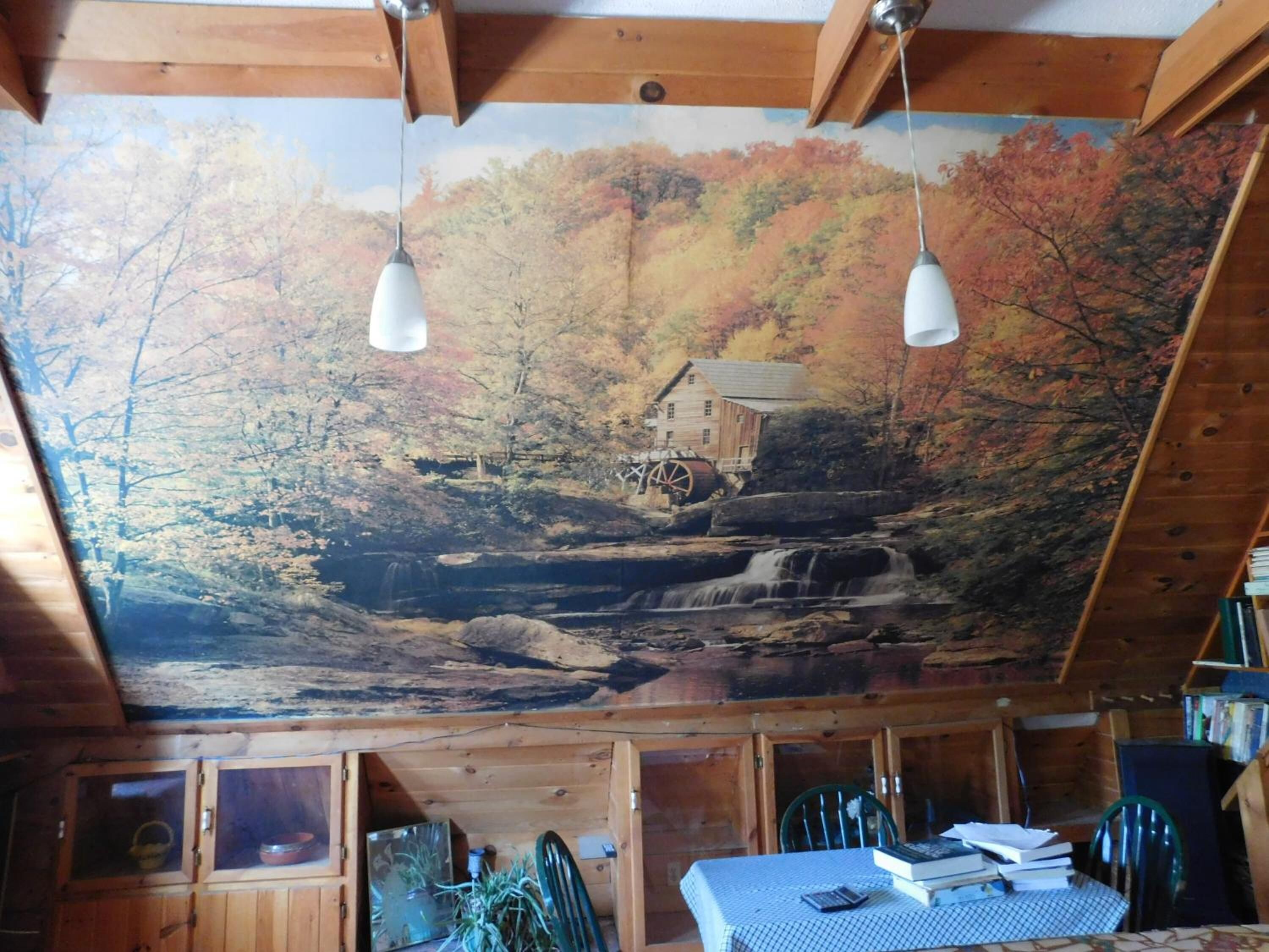 A rustic cabin interior with a mural of a waterfall and forest, wooden walls, and a table with books and papers.
